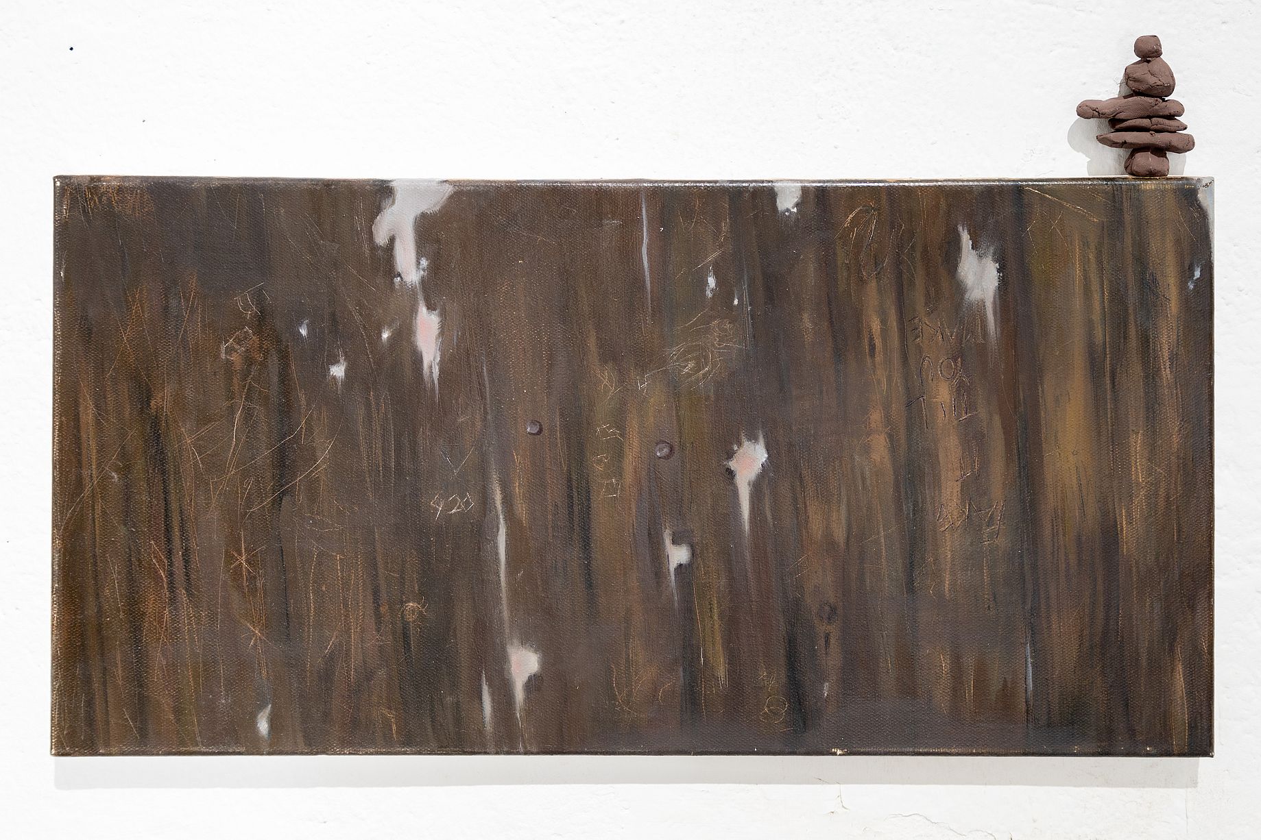 Obraz przedstawia abstrakcyjną kompozycję o ciemnobrązowej, przypominającej drewno fakturze z białymi i różowymi akcentami, a w prawym górnym rogu znajduje się mała rzeźba z ułożonych kamieni, przypominająca inuksuk.