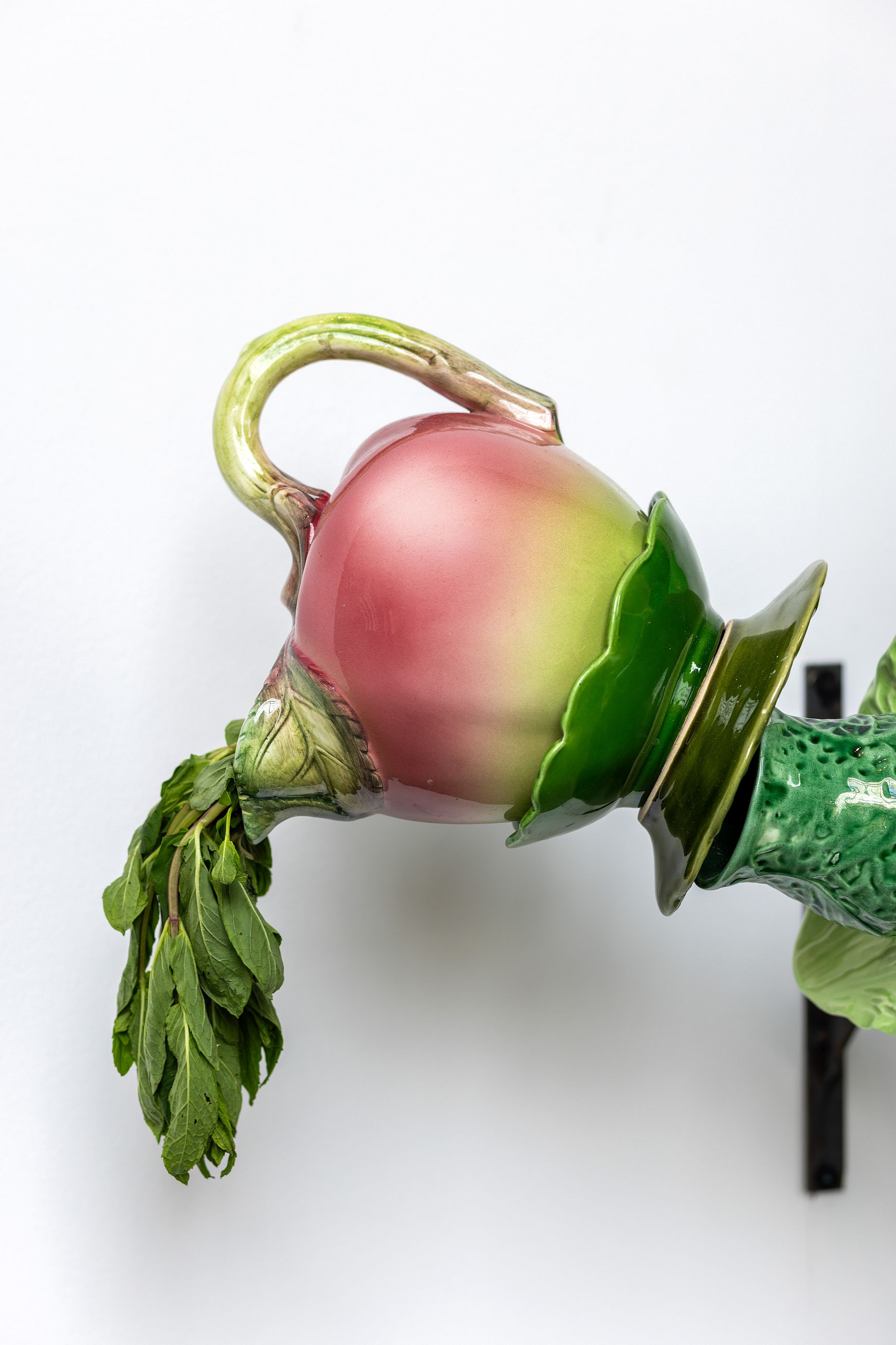 barwna i surrealistyczna rzeźba w kształcie łuku, ułożona z precyzyjnie balansujących na sobie kolorowych naczyń ceramicznych oraz świeżych warzyw, takich jak kapusta, brokuły i koper włoski.