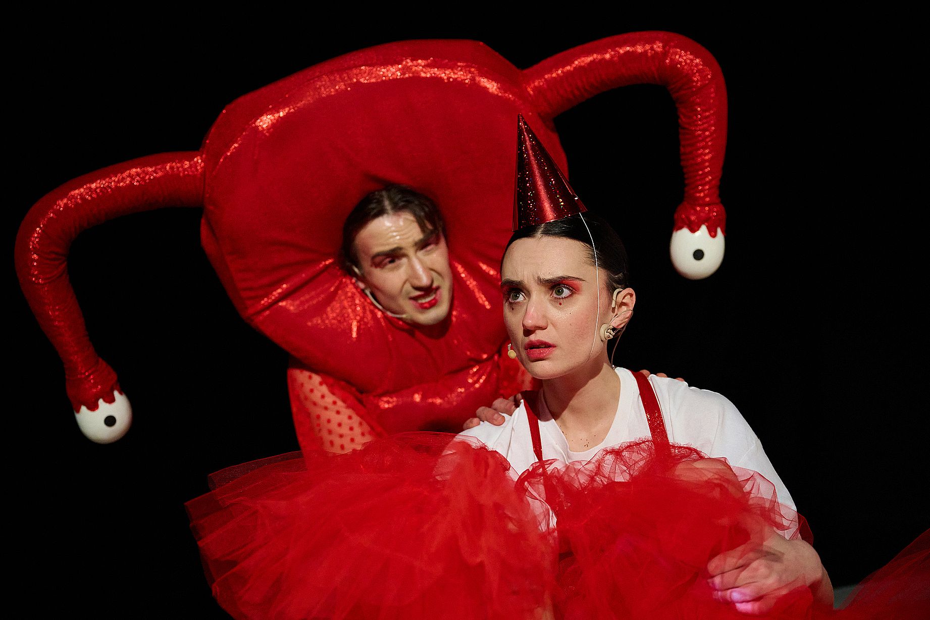 aktorzy na scenie teatru dla dzieci ubrani w czerwono białe stroje, mężczyzna w dziwnym nakryciu głowy