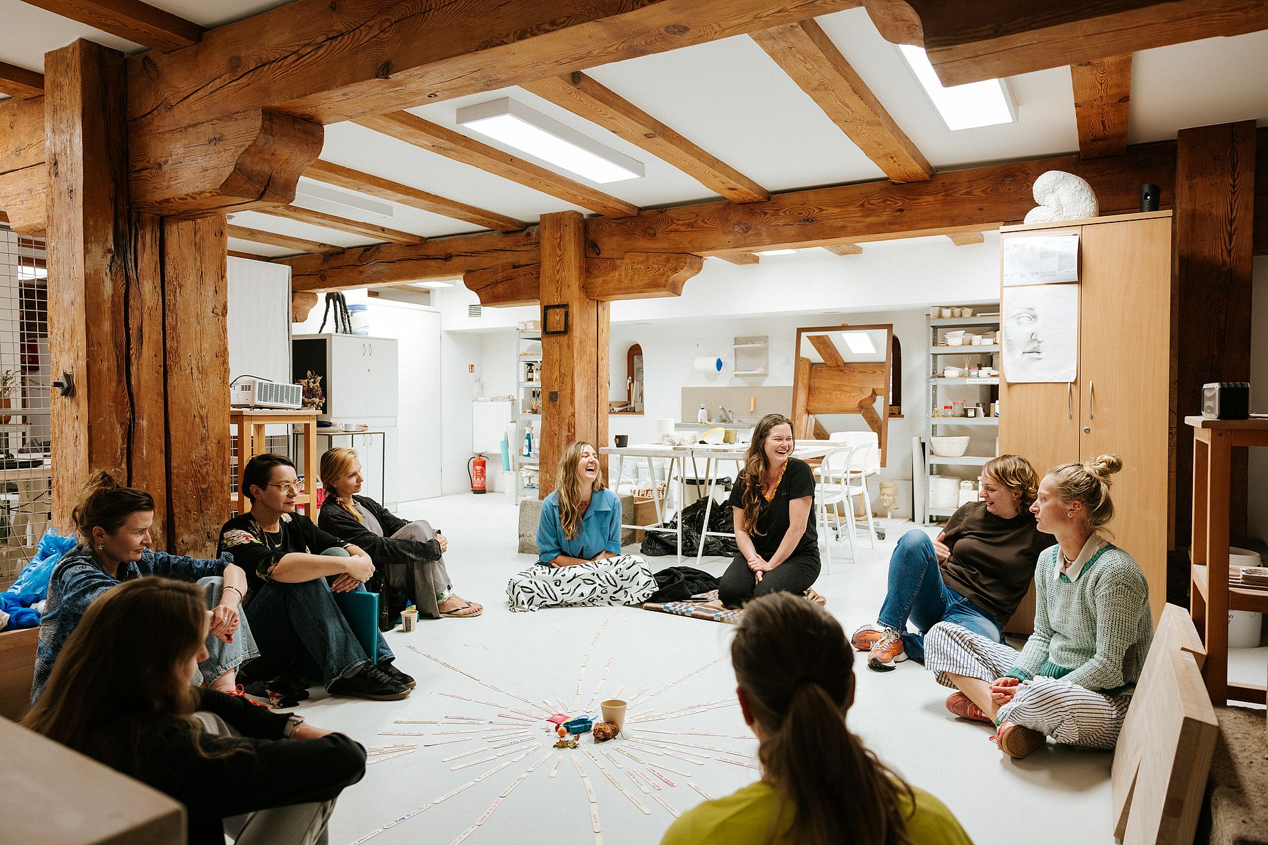 Spory krąg osób, kobiet siedzi na podłodze w kręgu, zapewne na warsztatach w galerii