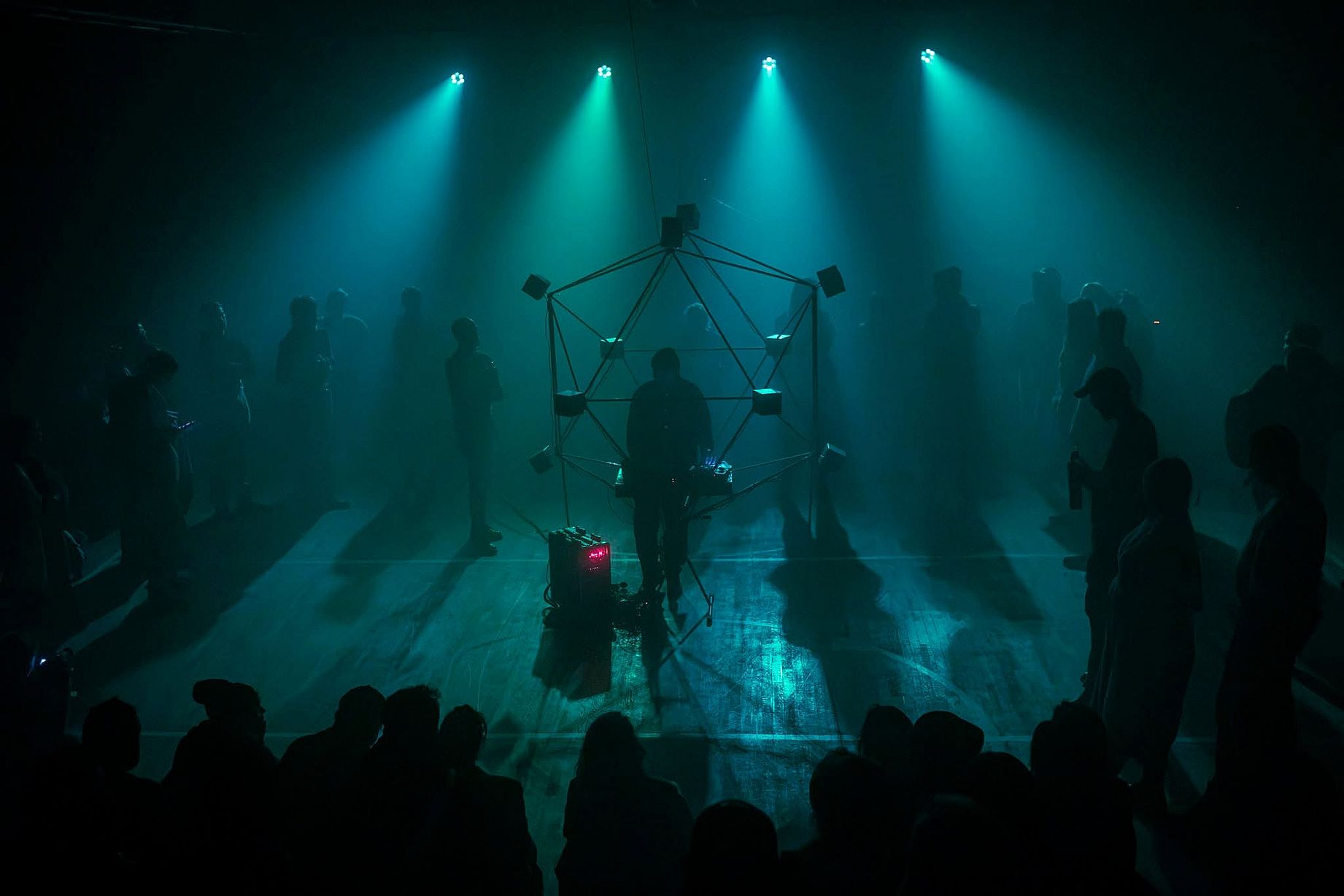 Scena teatralne, duzo ludzi, niebieskie światło, na środku dziwne rusztowanie