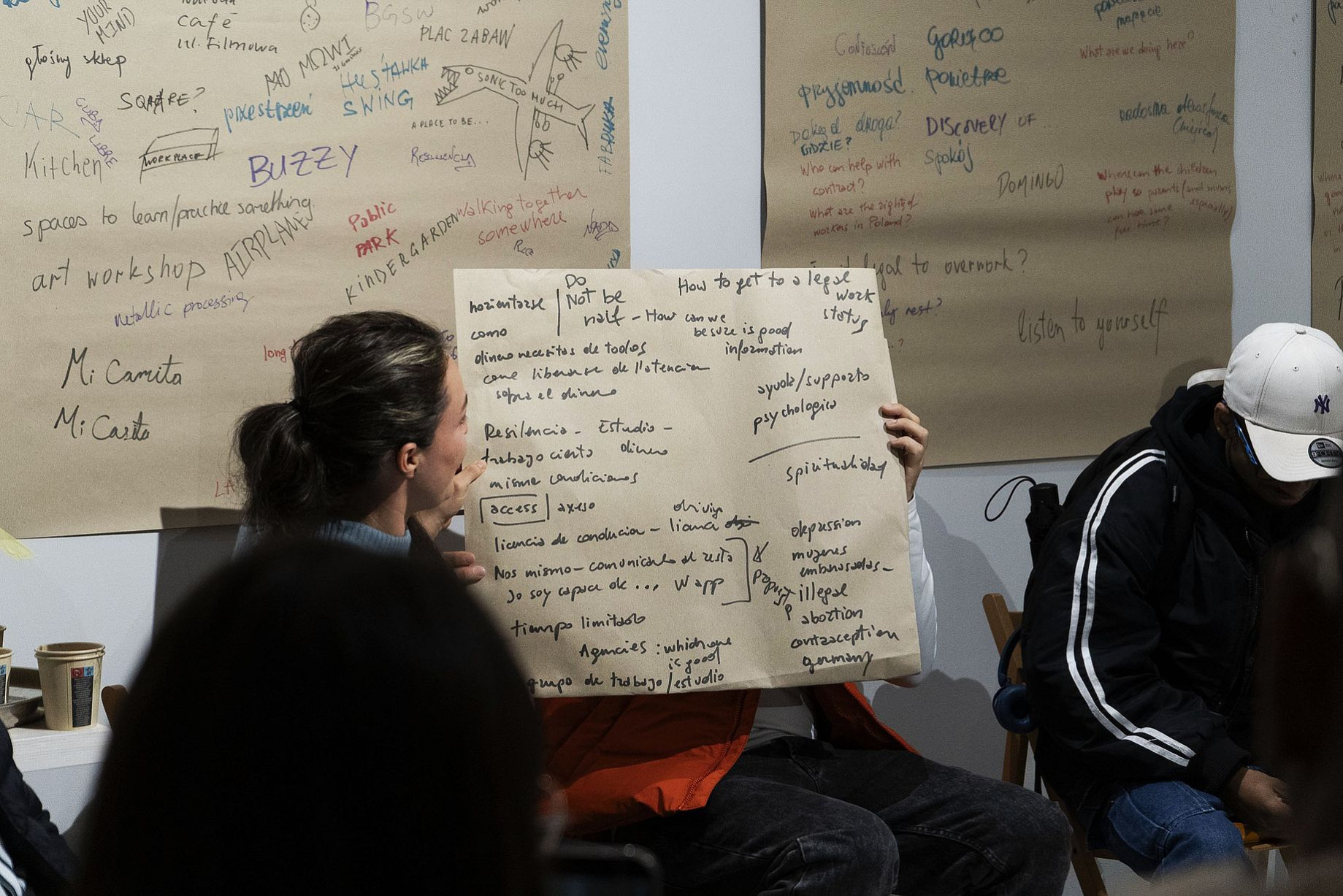 Warsztaty w galerii, osoba w środku trzyma duża plansze z napisami