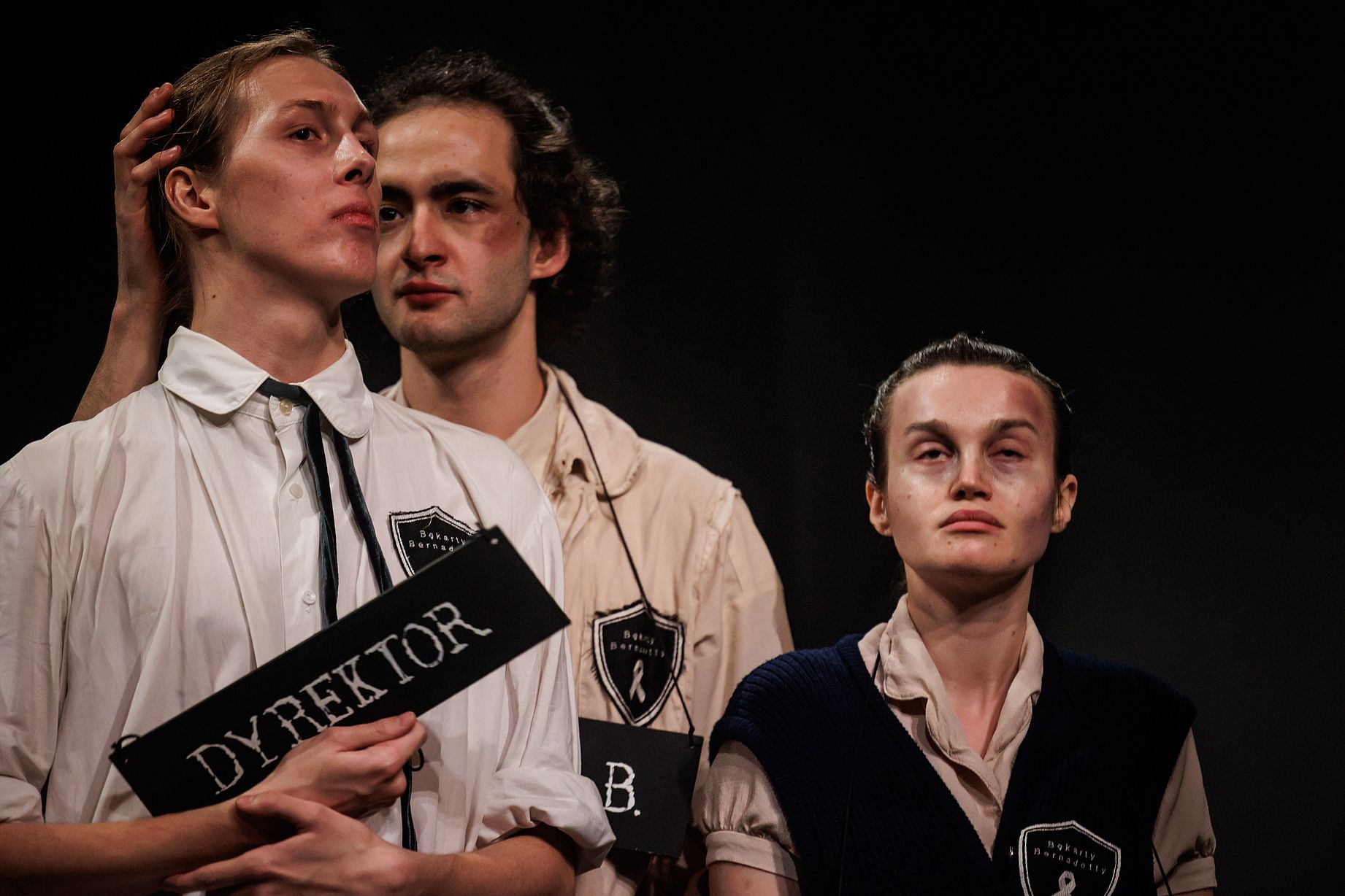 scena w teatrze rozgrywająca się&nbsp;szkole, mężczyzna trzena z głowe młodzieńca, który trzyma tabliczkę z napisem dyrektor, obok dziewnczyna, która wygląda jak po pobiciu