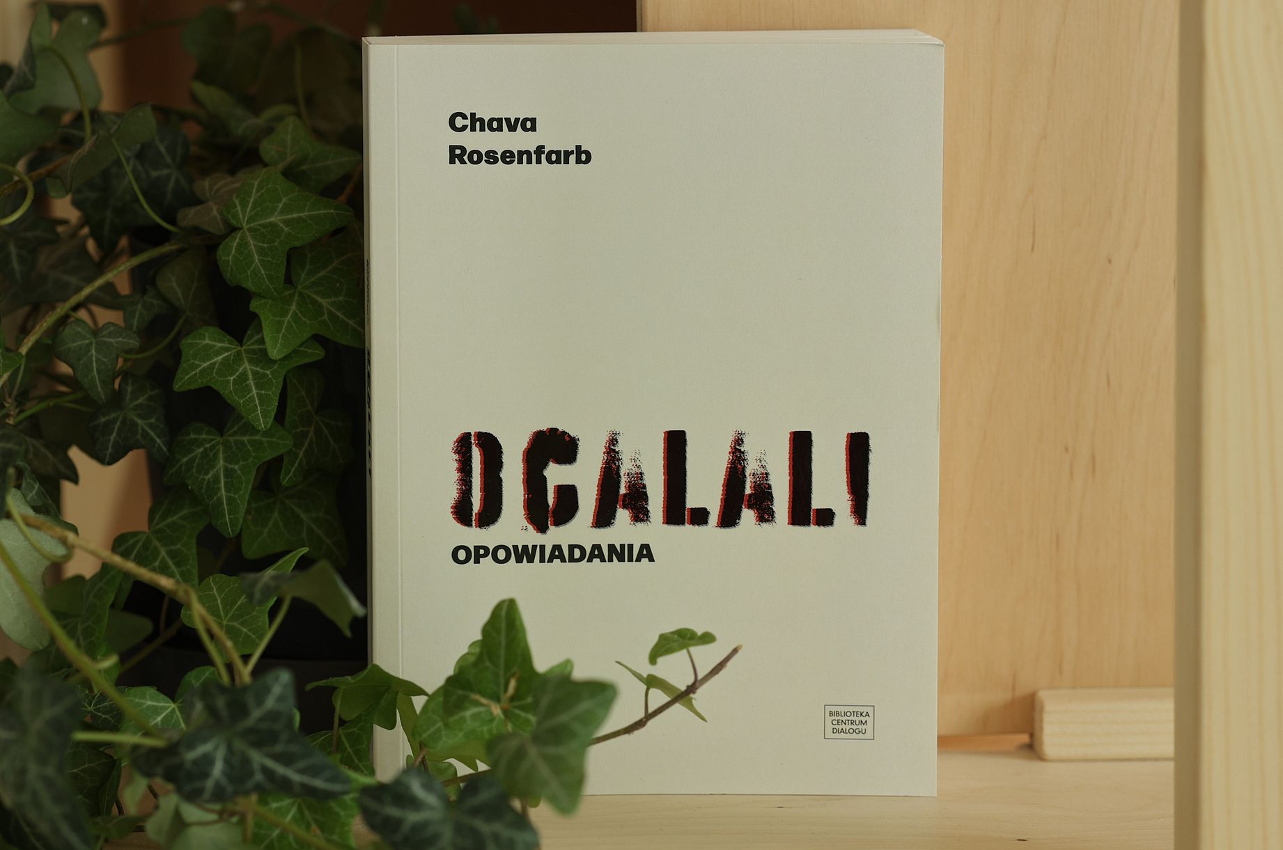 Książka z napisem Ocalali stoi na półce, obok rośliny