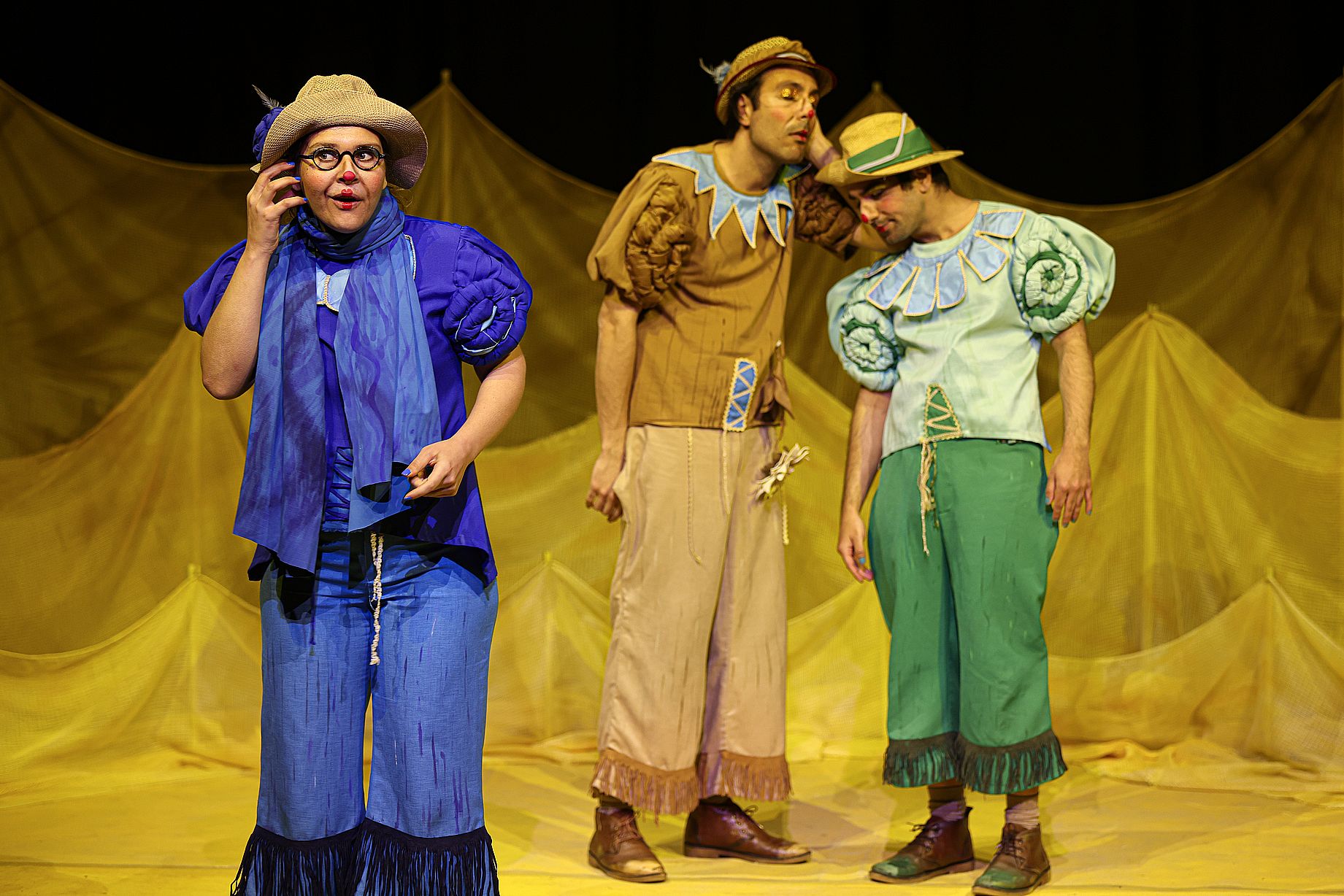 aktorzy teatru dla dzieci w kolorowych strojach, stoją na scenie, z żółta dekoracją, umalowana aktorka robi dziwną minę