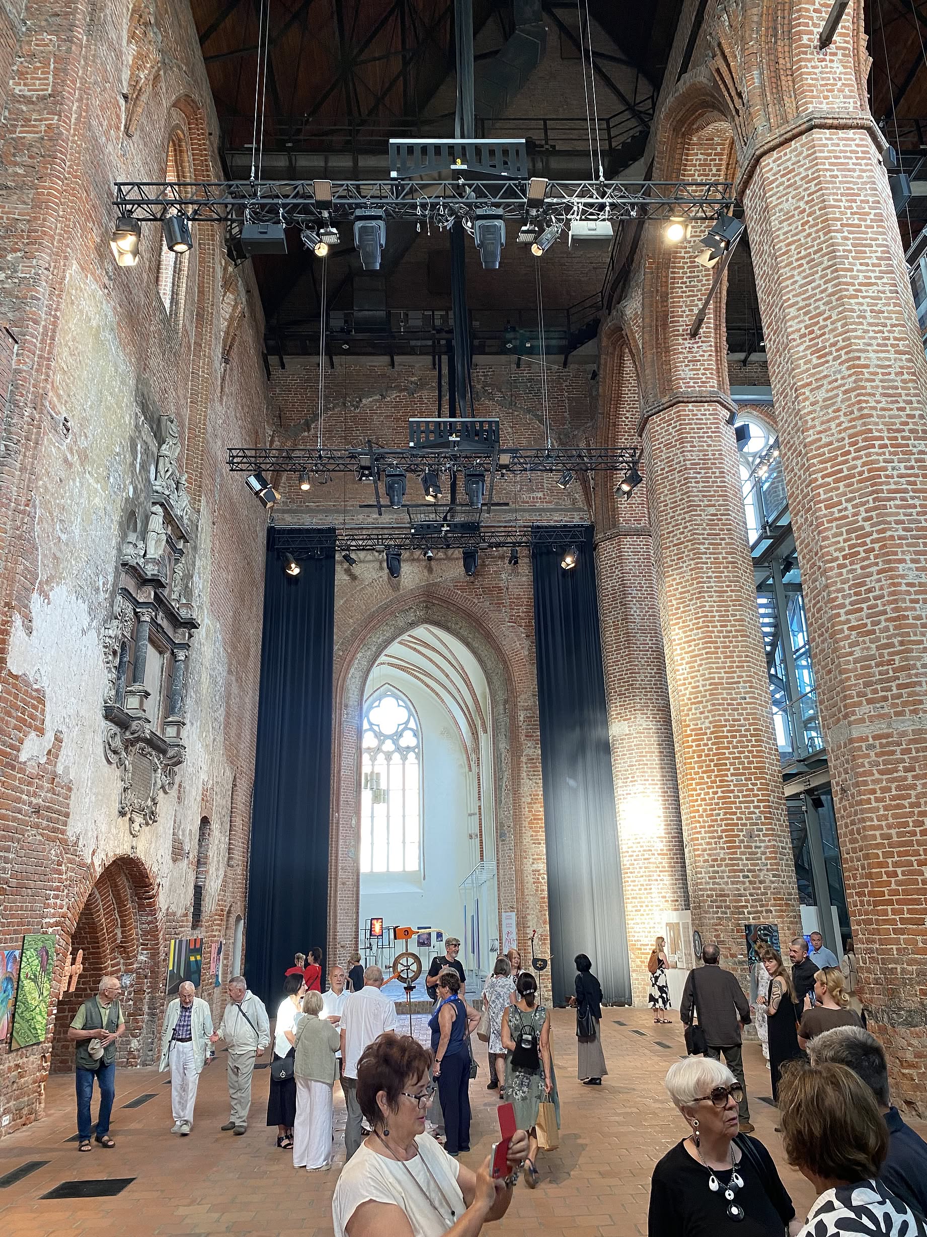 Wnętrze galerii sztuki, mieszczącej się w starym kościele, dużo ludzi, ogromna przestrzeń