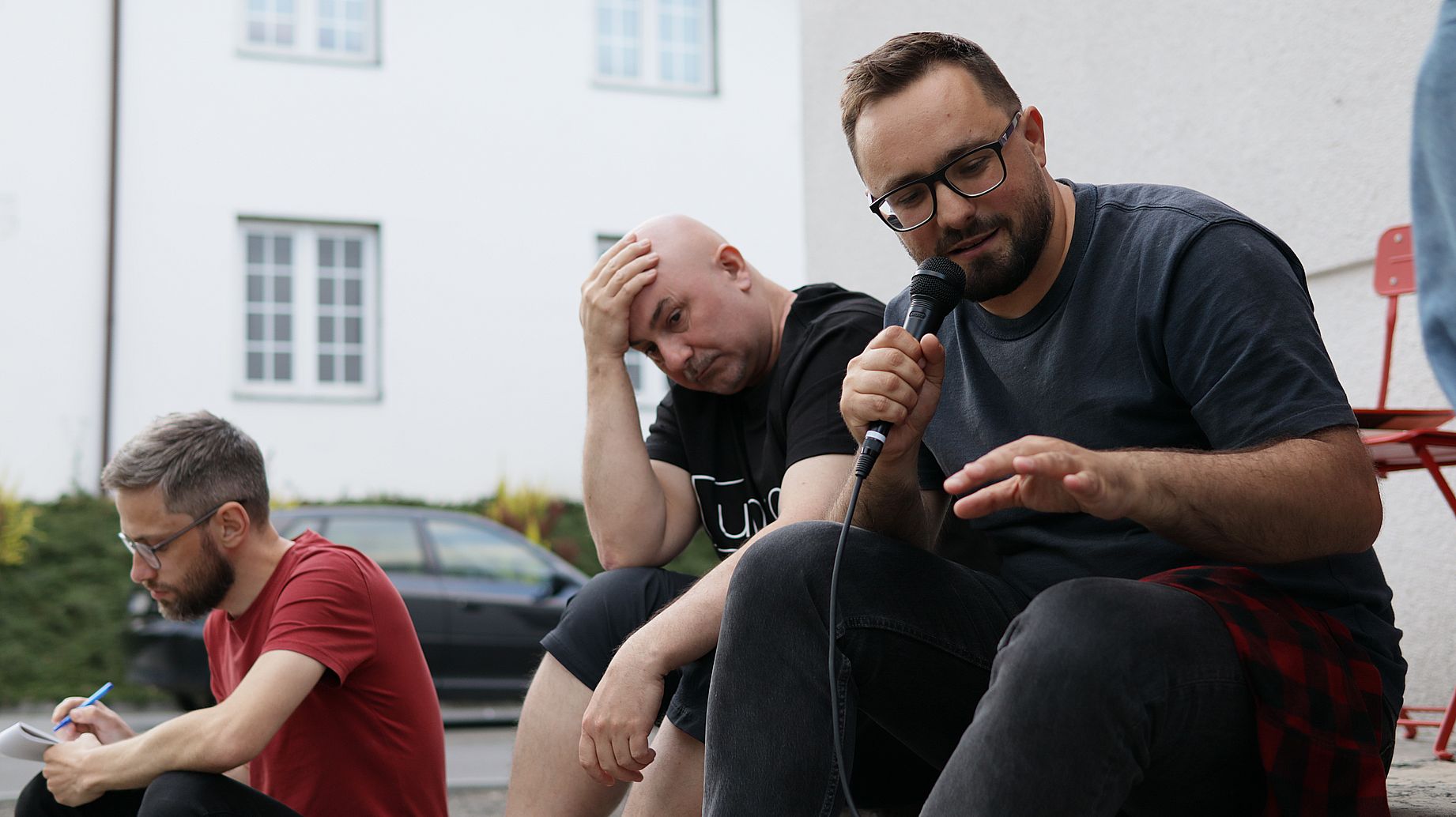 trzech mężczyzn siedzi na schodach, jeden mówi do mikrofonu