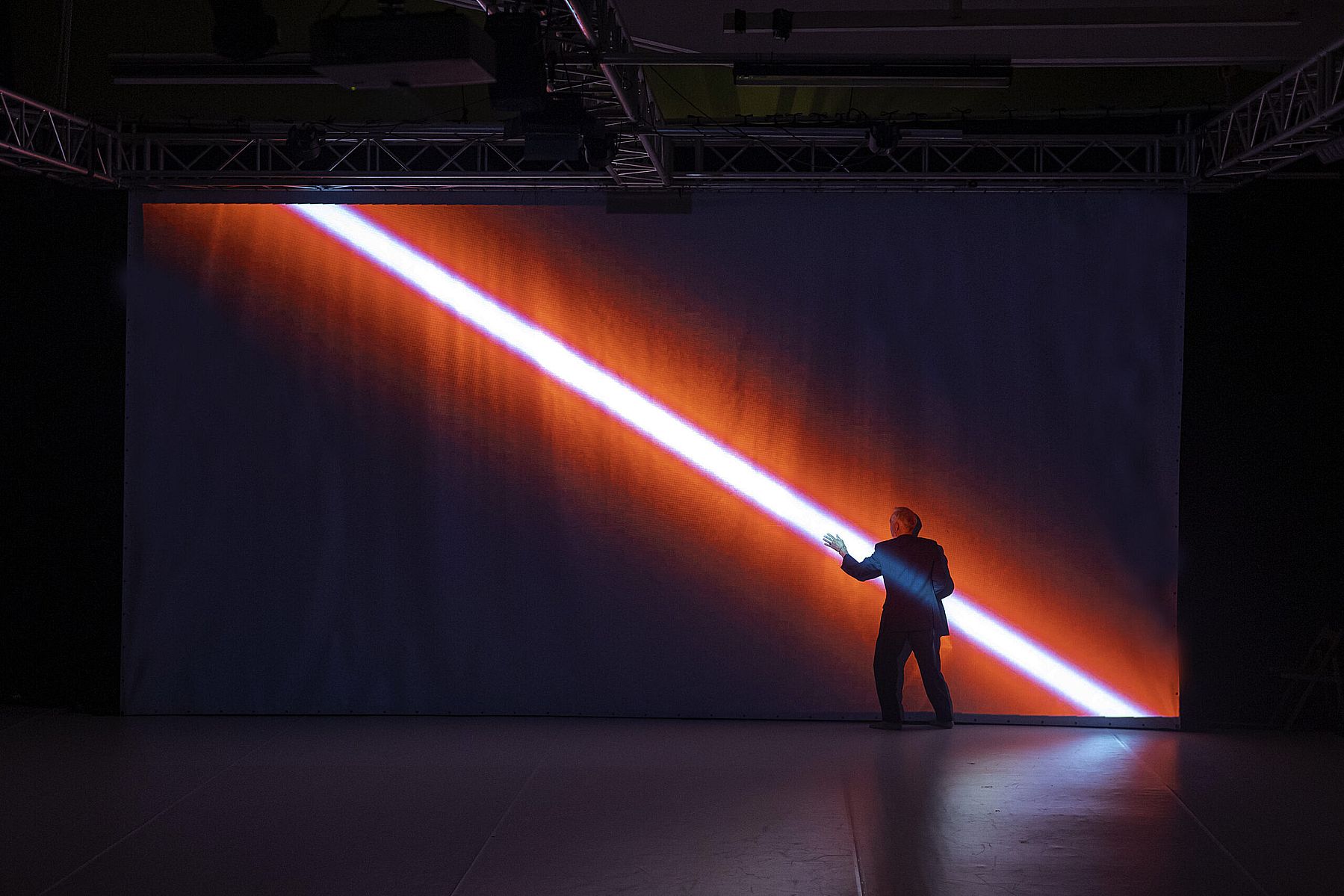 Mężczyzna na scenie przy kurtynie, przeszywa go czerwony promień światła