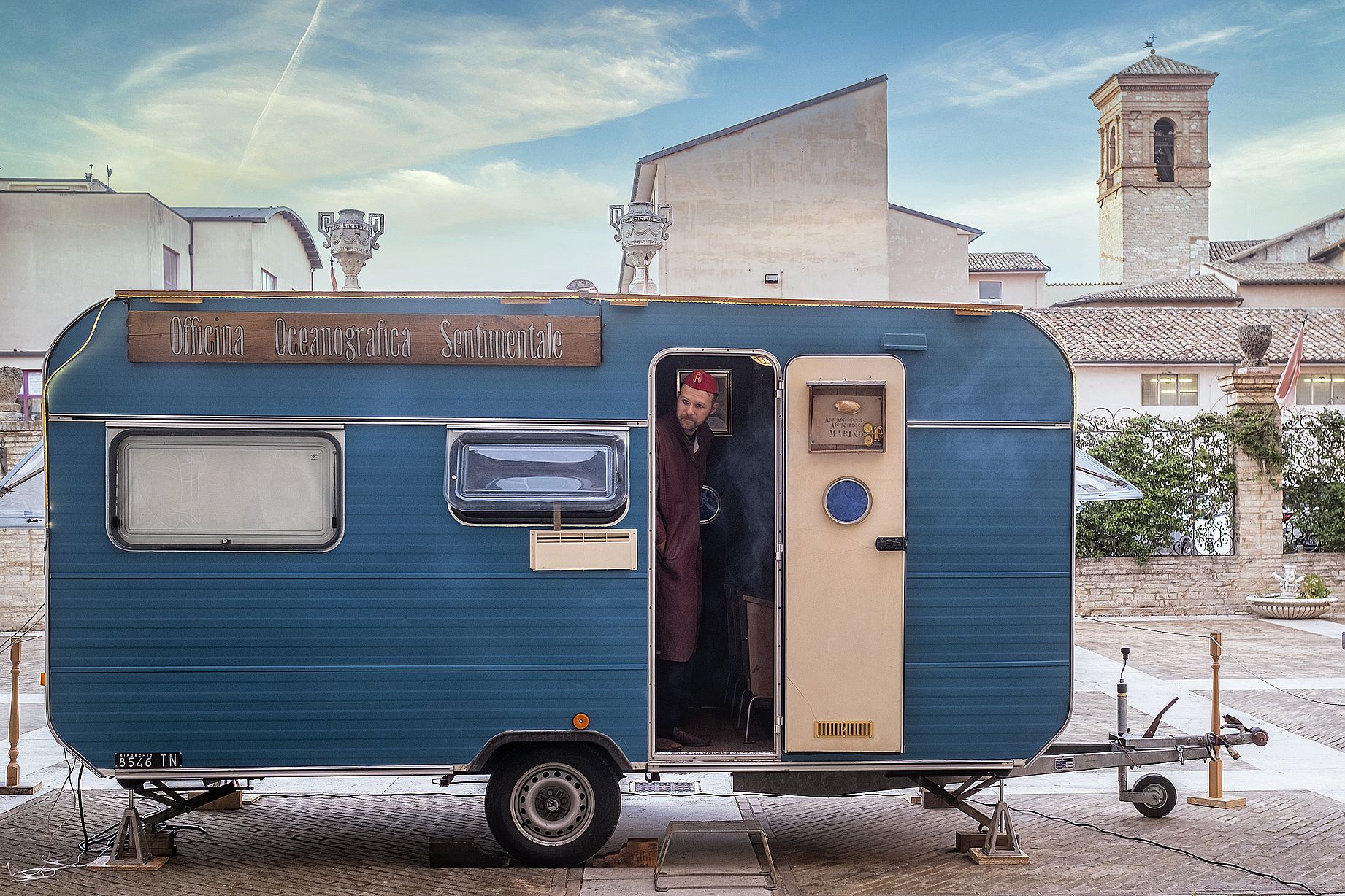 niebieska przyczepa, w drzwiach mężczyzna w czerwonej czapce