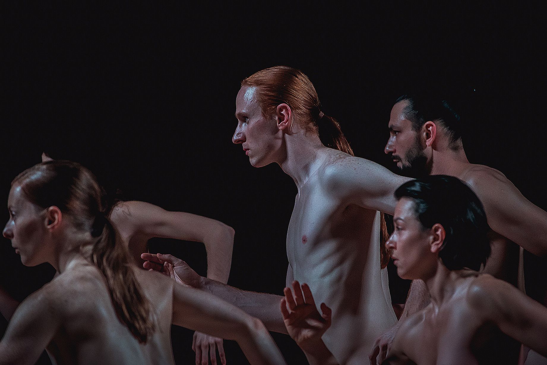 grupa pięciu tancerzy, gołe ciała skierowane w bok, na pierwszym planie rudy mężczyzna z długi włosami