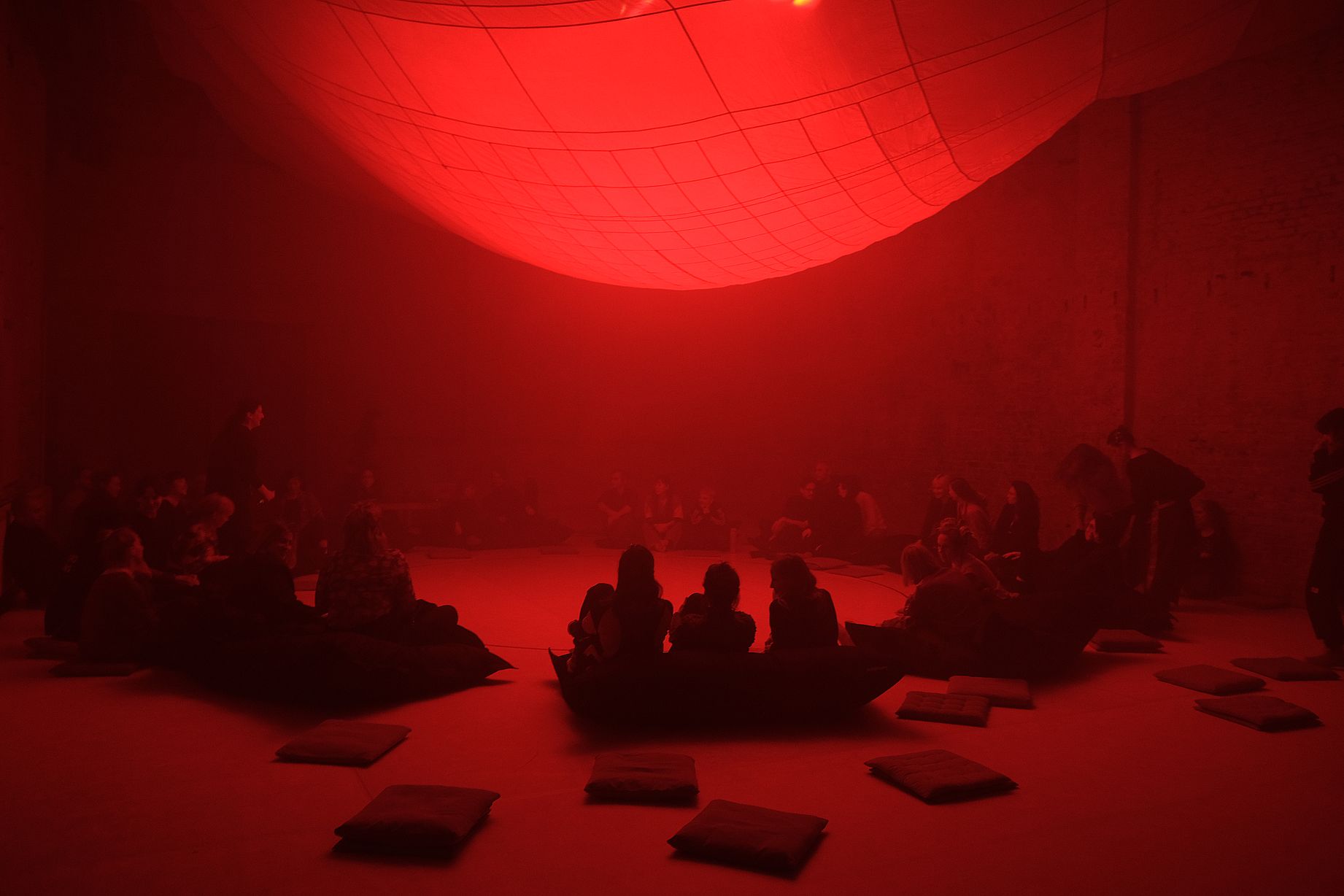 czerwona kula, czerwone światło, w sali dużo publiczności siedzącej na podłodze
