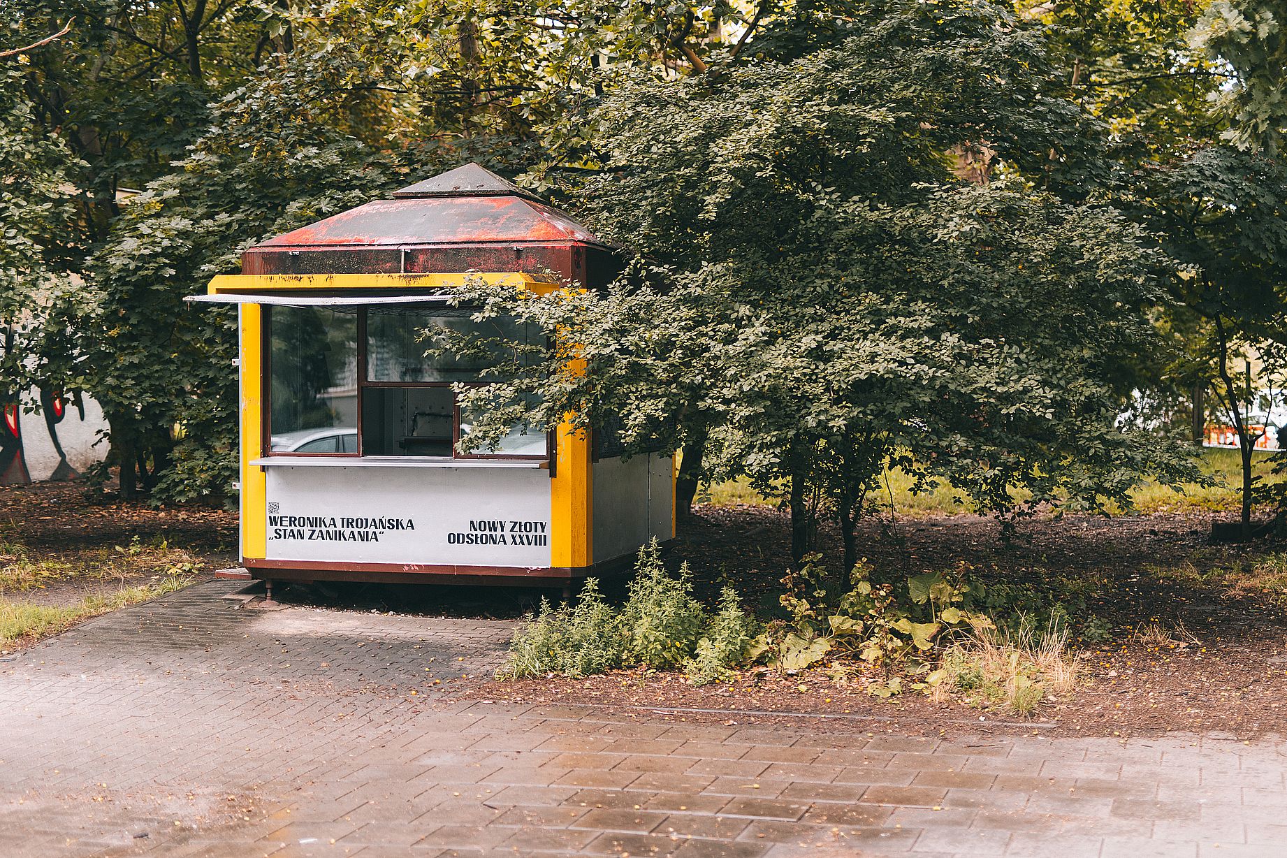 Żółty kiosk, przerobiony na galerię sztuki, w tle dużo zieleni