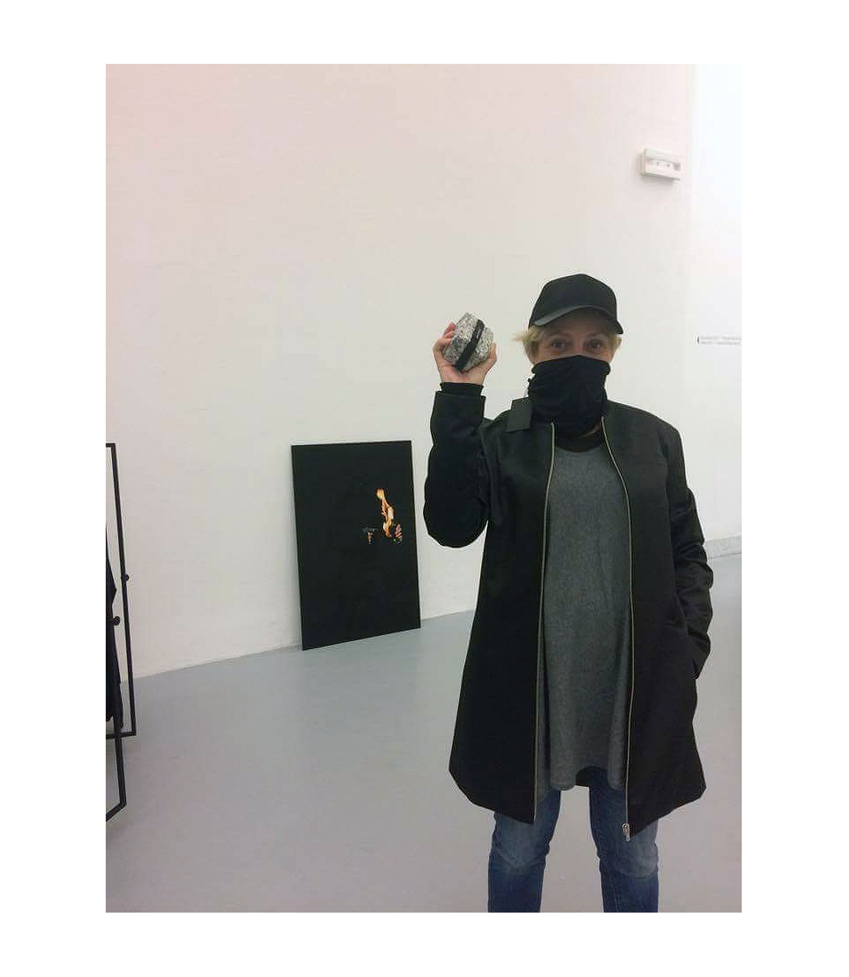 kobieta stoi w galerii sztuki, jest lekko zamaskowana, w reku trzyma jakiś przedmiot