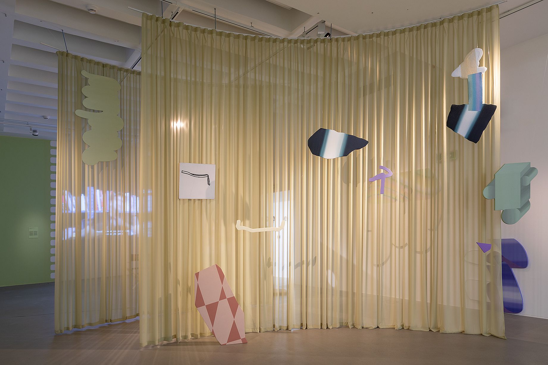 pofałdowana kotara, a na niej kolorowe prace w dziwnych kształtach