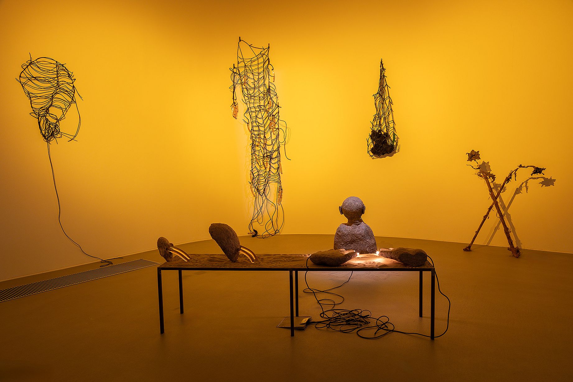 Widok wystawy, posąg buddy na stole, instalacje w włóczki, żółte, nastrojowe światło