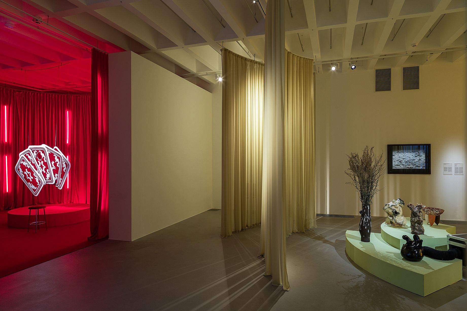 widok wystawy, ekran, ceramika po prawej, żólte światło, po lewej czerwona poświata, wiszące duże karty do gry