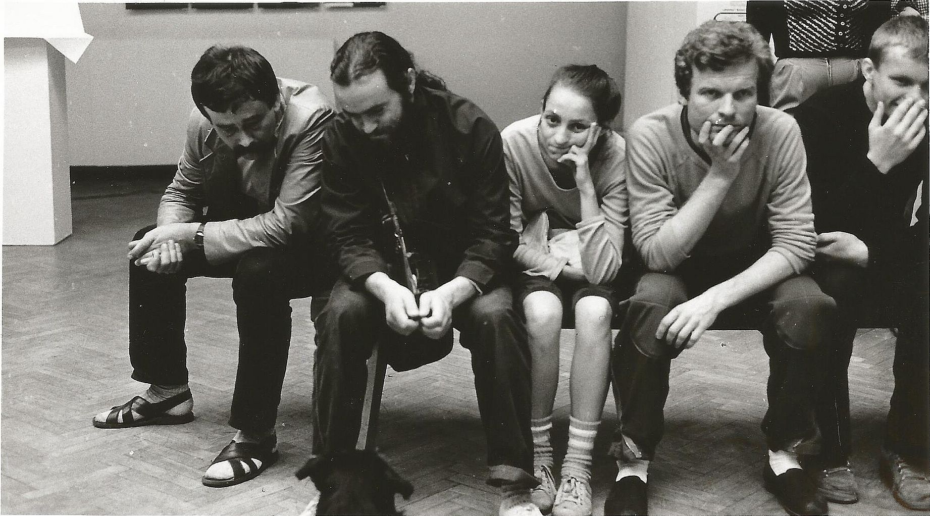 cztery osoby siedza na ławce w galerii, patrzą na psa