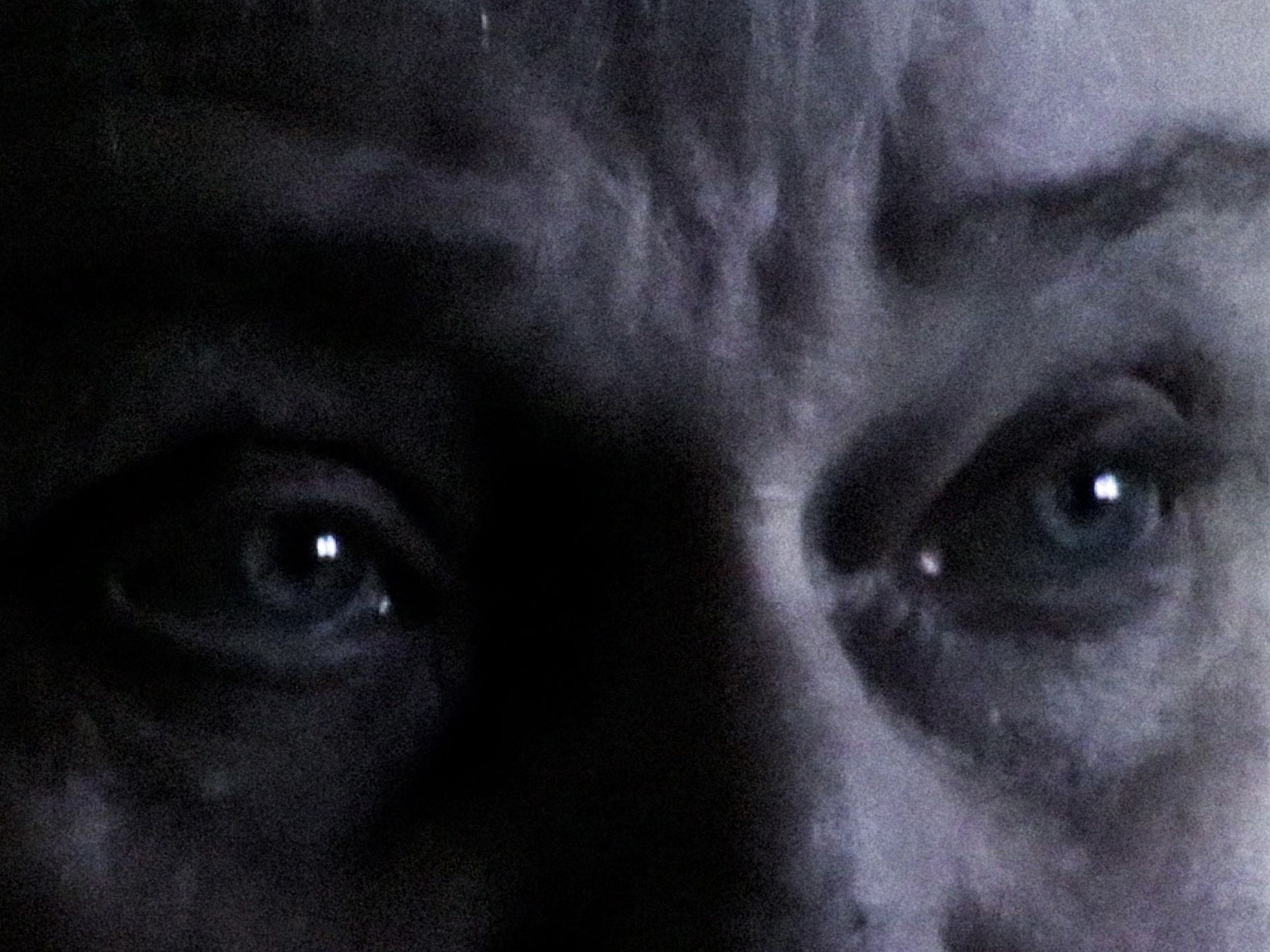 Zbliżenie ukazuje parę szeroko otwartych, niebieskich oczu i zmarszczone czoło osoby w bardzo słabym, mrocznym oświetleniu, co sugeruje intensywny strach lub niepokój