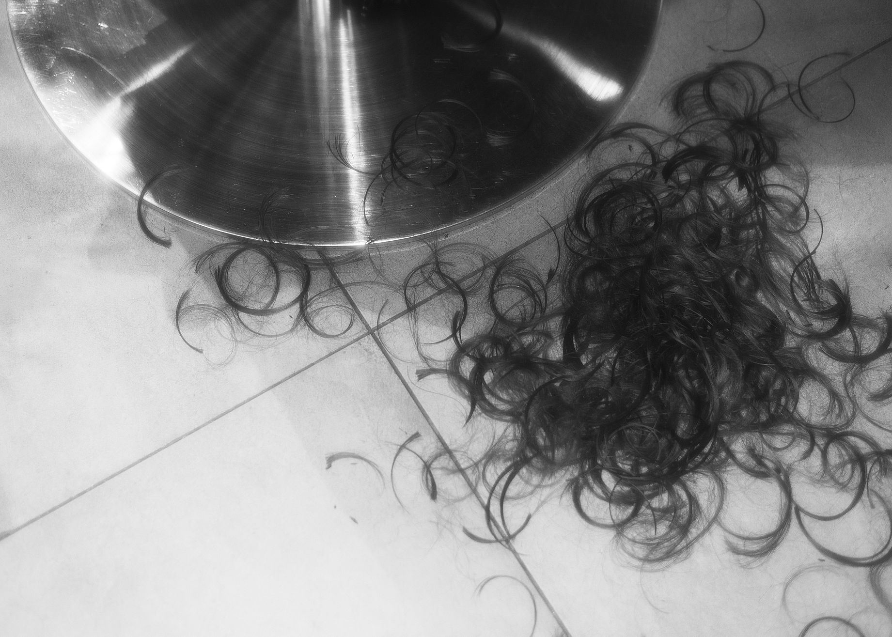 czarno-białe zdjęcie przedstawiające podłogę w zakładzie fryzjerskim, ścięte włosy