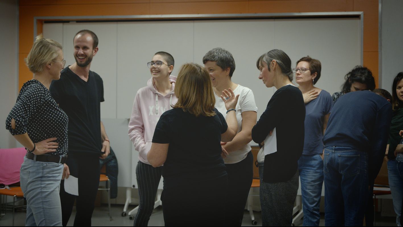 Grupa dorosłych osób stoi w sali warsztatowej, rozmawiając i śmiejąc się w swobodnej, przyjaznej atmosferze.